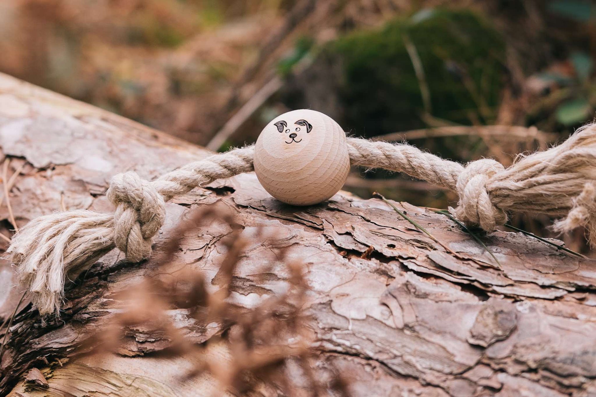 Smug Mutts Tug-a-Ball Natural Hemp and Beech Wood Dog Toy Resting on a Log