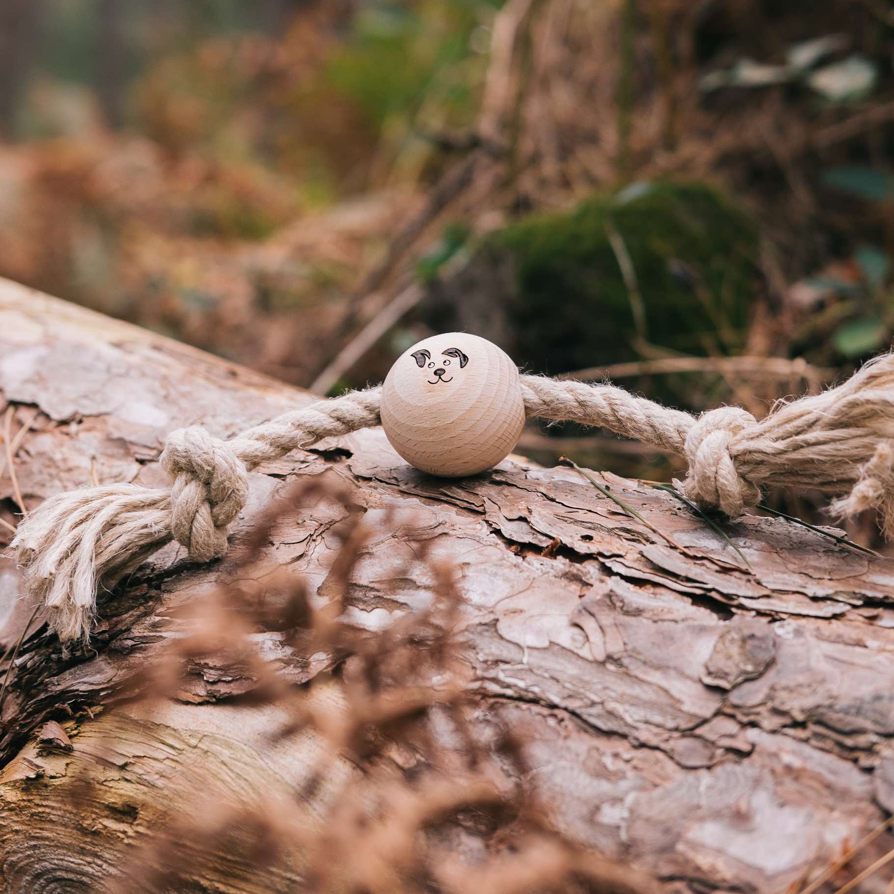 Smug Mutts Tug-a-Ball Natural Hemp and Beech Wood Eco Friendly Dog Toy Resting on a Log, All Handmade in the UK and 100% Plastic Free